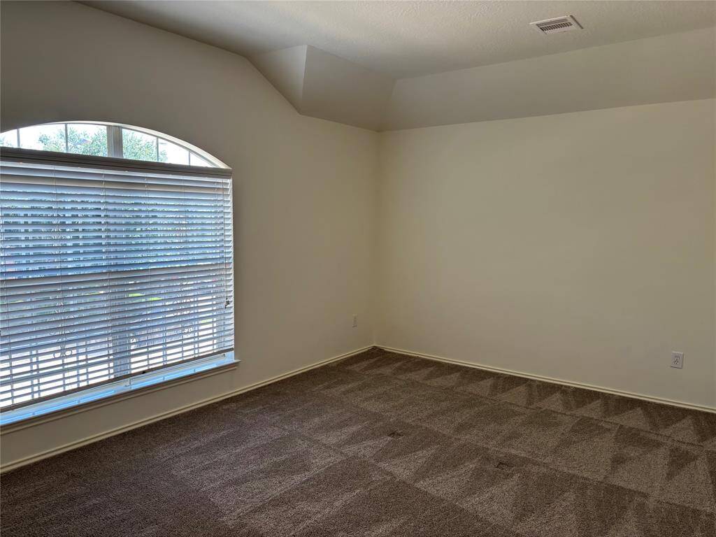 This game room upstairs features neutral walls and carpet, with a large arched window providing natural light and a view outside.