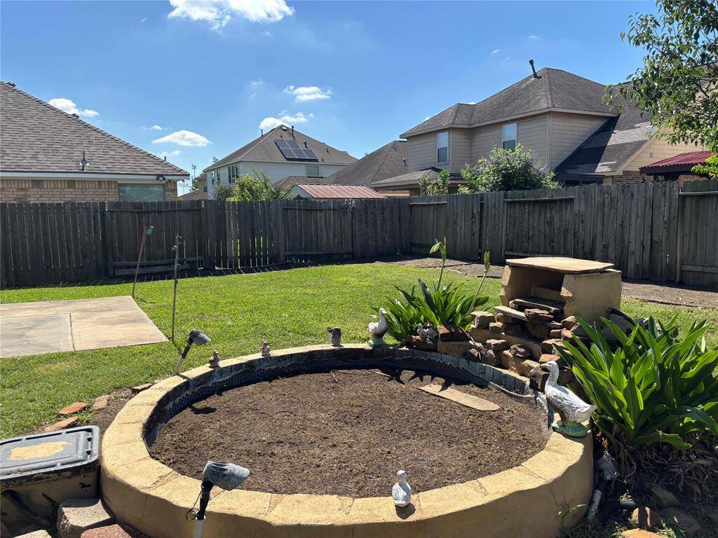 This backyard features a grassy area with a circular garden bed, surrounded by a wooden fence for privacy. There is a small paved section and a simple brick structure, providing a versatile outdoor space.