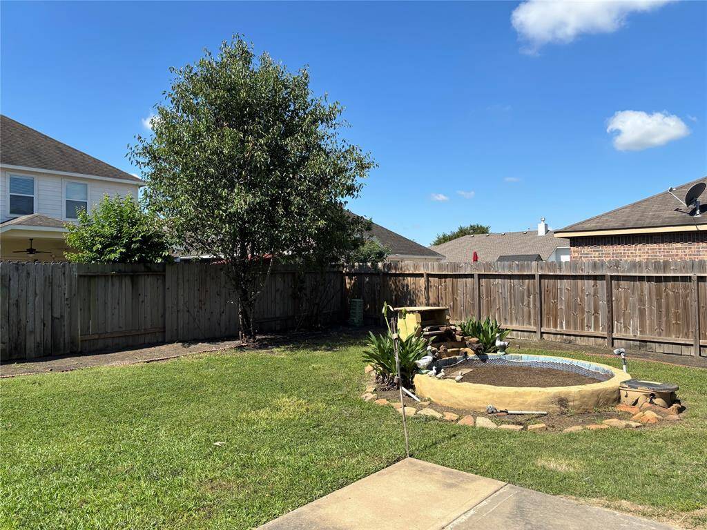This backyard features a well-maintained lawn with a small garden pond, surrounded by a wooden fence for privacy. A mature tree provides shade, creating a serene outdoor space perfect for relaxation or entertaining.