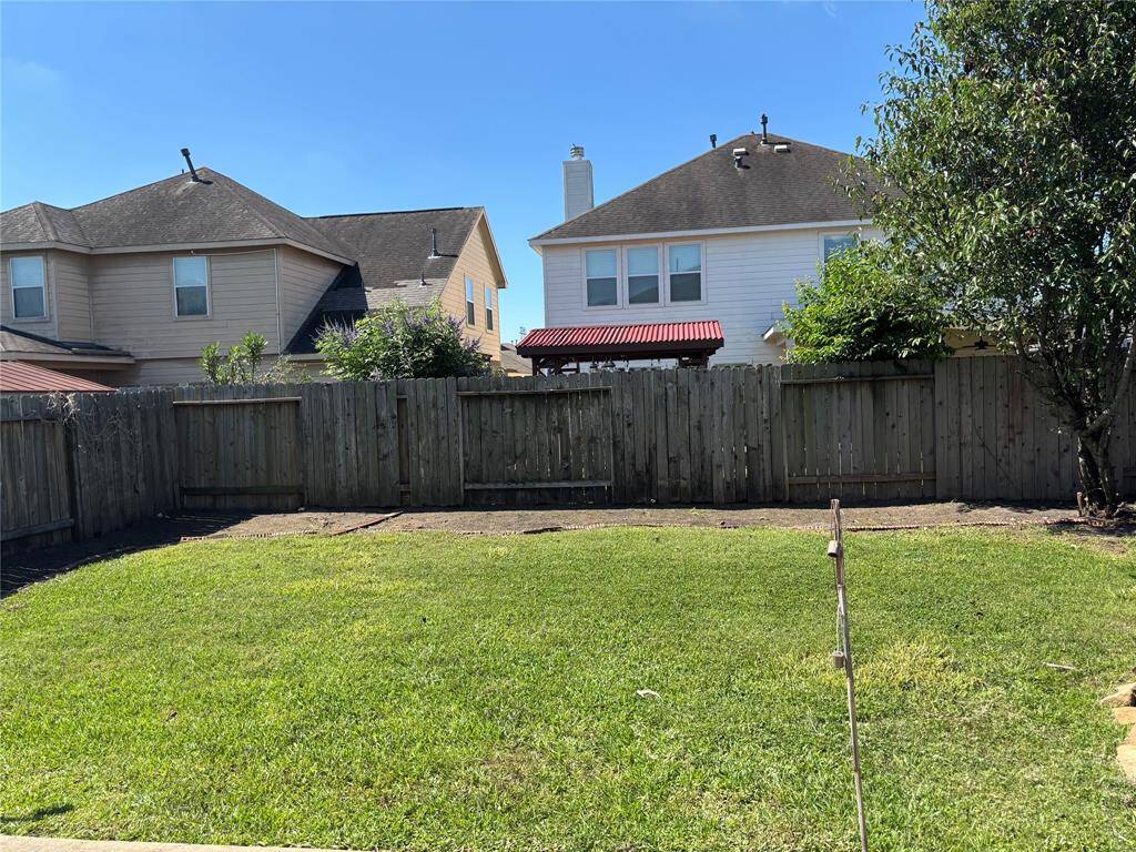 This photo shows a fenced backyard with a well-maintained lawn, bordered by neighboring houses. The space offers potential for landscaping or outdoor activities.