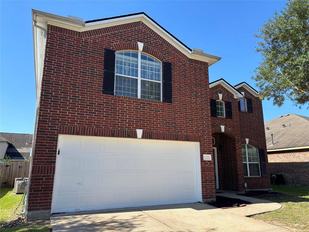 This photo shows a two-story brick home with a double garage and large arched windows. It features a well-maintained exterior with black shutters and a small front garden area.