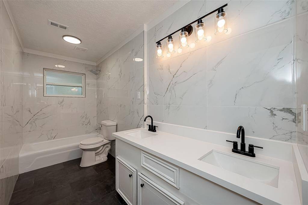 Completely remodeled secondary bathroom with a dual vanity and tile wall all throughout.