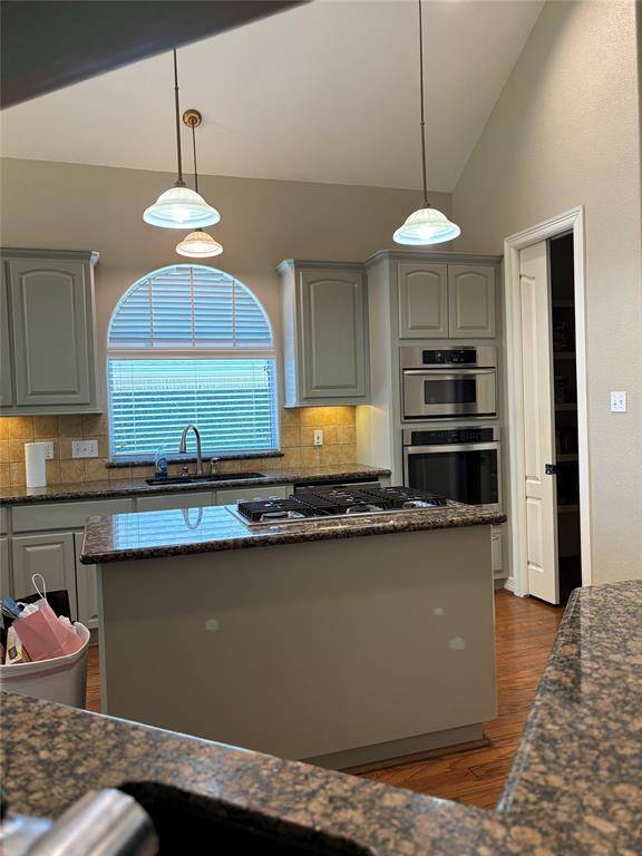 The room is entered through a gracefully arched opening, giving it a formal and inviting feel. It features a vaulted or tray ceiling, adding height and a sense of spaciousness to the room. A central chandelier hangs down, providing both illumination and a touch of classic style. The space is lined with large, arched windows that let in abundant natural light. These windows offer a beautiful view of the front yard with lush greenery and a street