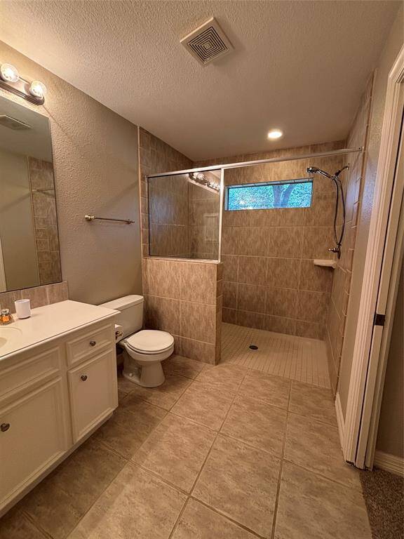 This bathroom boasts a spacious walk-in shower with a glass partition, elegant tiled surfaces, a sleek white vanity with a large mirror, and stylish modern lighting.