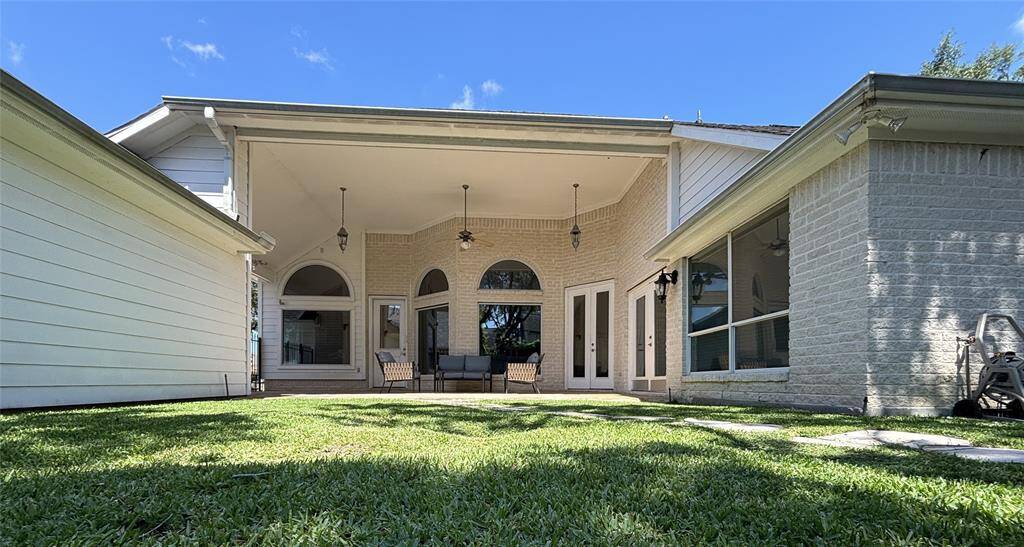 The rear of the home shows a beautiful covered patio with high ceilings, beautiful arched windows, and French doors that open into the living space. The brick exterior and flagstone flooring create a warm, elegant outdoor living area.