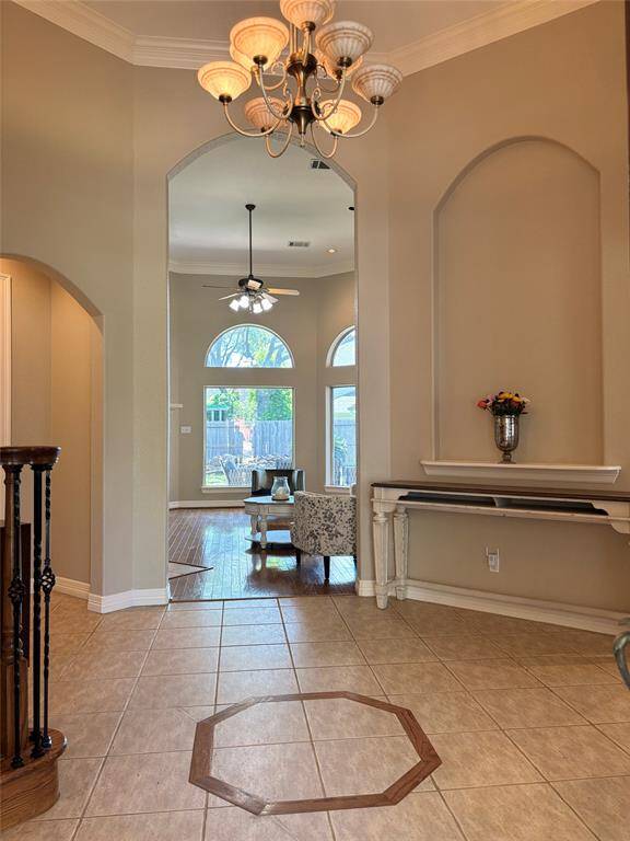 This photo shows a welcoming hallway with warm wood flooring, an elegant archway, and a staircase leading to the second floor. The space is well-lit with a niche light and opens to a bright room with large windows.