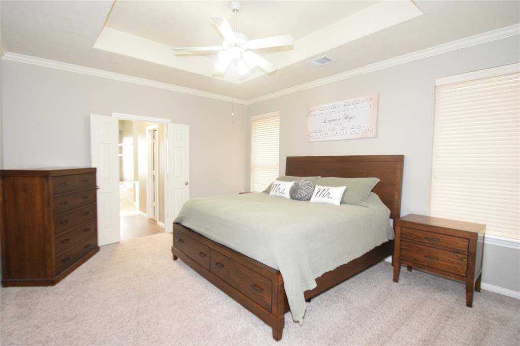 Primary bedroom complimented by raised ceilings, crown molding and a ceiling fan with light fixture.