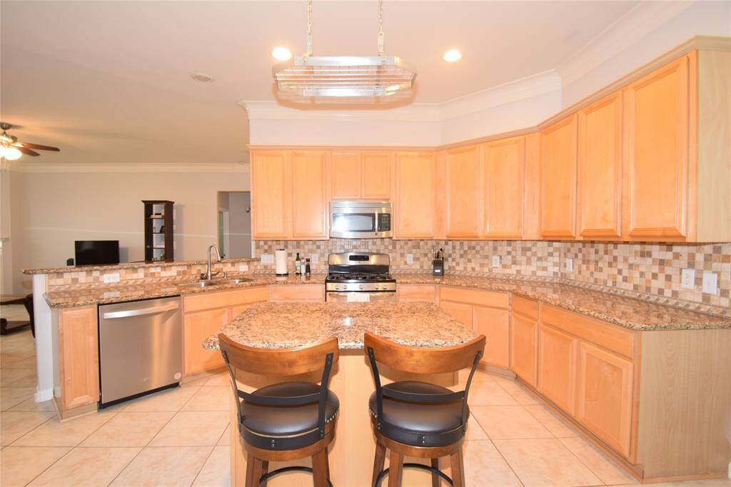 Kitchen offering tile floors, granite counter tops, tile backsplash, gas cooking, built-in microwave and island workspace with a breakfast bar.