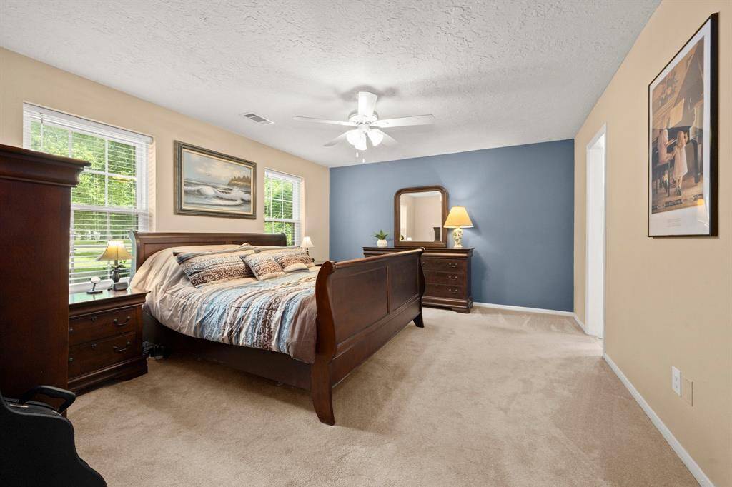 First floor primary suite showcases a neutral and soothing color pallet, plush carpe, ceiling fan and accent wall.