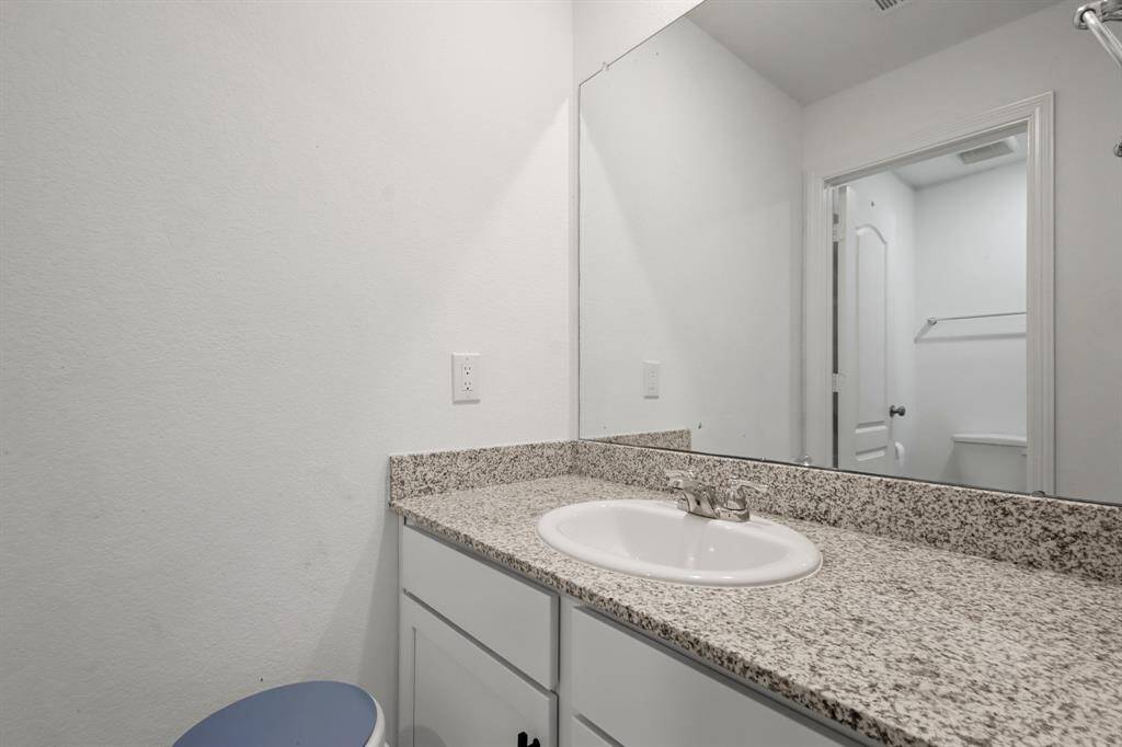 Secondary bathroom with granite countertops and backsplash, wooden cabinetry, and a large mirror.