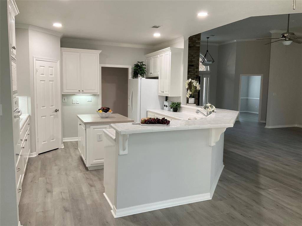 The kitchen has been updated with a new dishwasher, garbage disposal, refrigerator and an ideal space for a wine refrigerator. Freshly painted white cabinetry, a large island, and lots of kitchen cabinet space. The open layout flows into a bright living area, accentuated by recessed lighting and a ceiling fan.