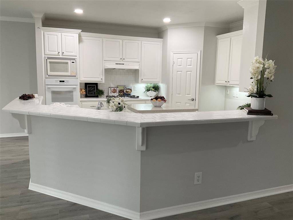 Updated kitchen with freshly painted white cabinetry, built-in appliances, and a spacious, tiled breakfast bar. The neutral color palette and recessed lighting create a bright and inviting atmosphere.  You see the beautiful outdoors in every direction.
