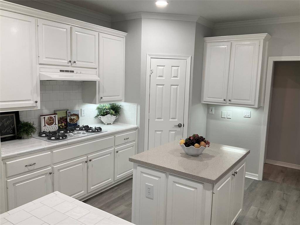 This kitchen features a modern design with white cabinetry, a central island, sleek countertops, recessed lighting, a built-in stove and ample cabinet storage space.  A delightful bright and functional space for cooking and entertaining.