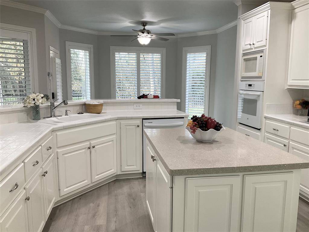 Bright and spacious kitchen with modern white cabinetry, an island, and stainless steel appliances. Large windows with shutters allow natural light, and there's ample counter space for cooking. The open design is perfect for entertaining.  Don't miss the large walk in pantry.