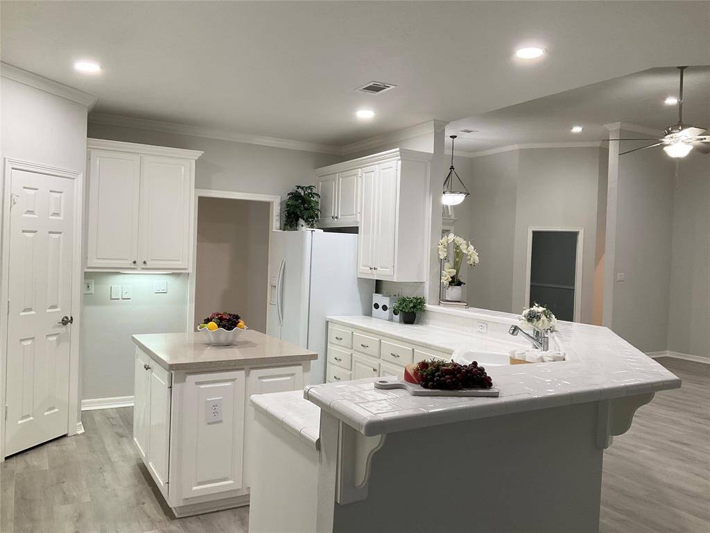 This kitchen features a modern, open layout with white cabinetry and a large island. It includes ample counter space, recessed lighting and an ideal location for a wine refrigerator. The neutral tones, recessed lighting, huge walk in pantry are a few of the kitchen highlights.