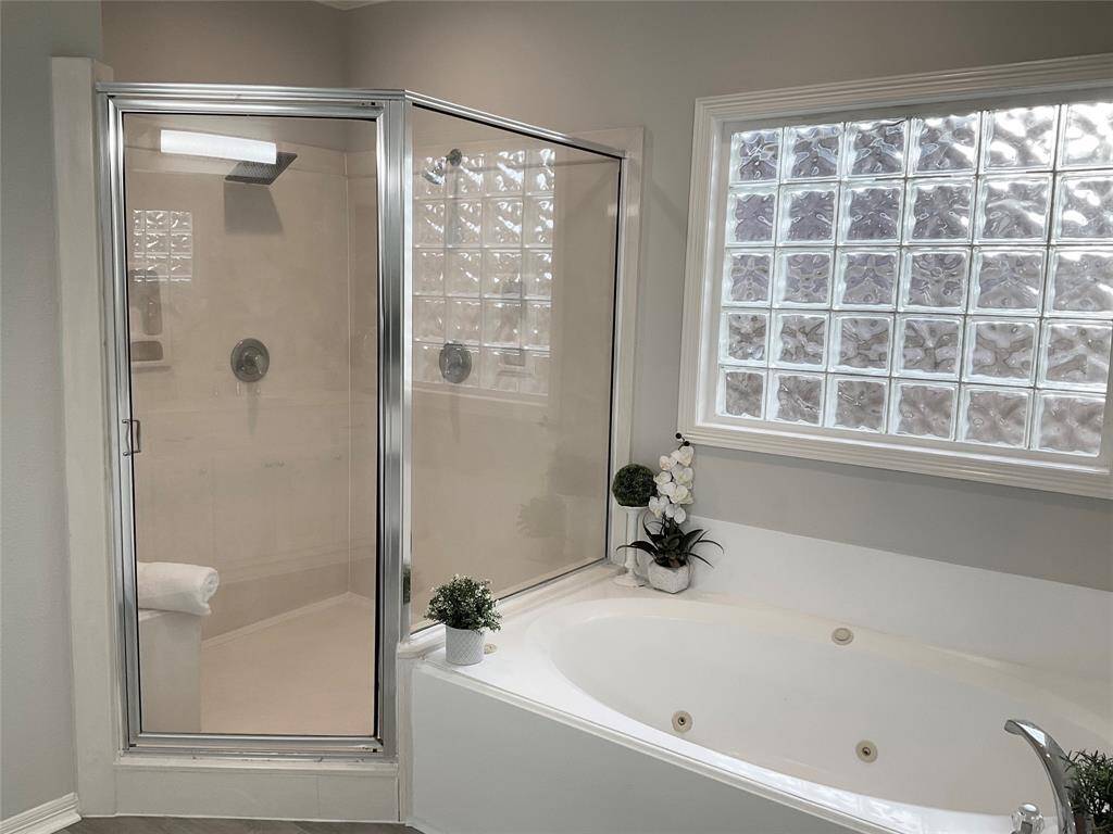 This bathroom features a glass-enclosed shower adjacent to a large soaking tub with sleek fixtures. It is well-lit by a decorative glass block window, creating a bright and inviting space.  Don't miss the double shower heads and bench in the shower.