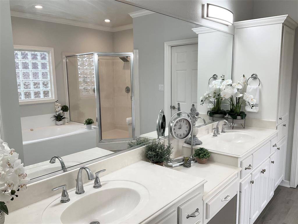 This bathroom features a dual-sink, vanity with modern light fixtures, ample cabinetry and a nice space for a vanity bench. It includes a glass-enclosed shower, a separate bathtub, and soft lighting for a relaxing atmosphere.