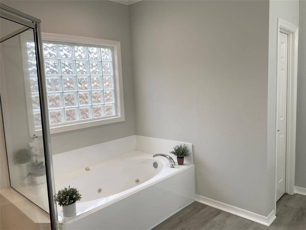 Bright bathroom with a modern design, featuring a spacious bathtub, glass block window for natural light, and new flooring.  A few neutral color bathroom rugs and you are all set for low maintenance.