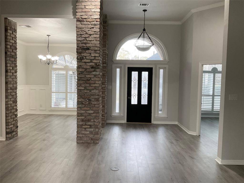 This entryway features a modern open layout with elegant brick columns, light, vinyl, durable, wood flooring, and abundant natural light. A stylish chandelier and arched windows complement the inviting atmosphere.