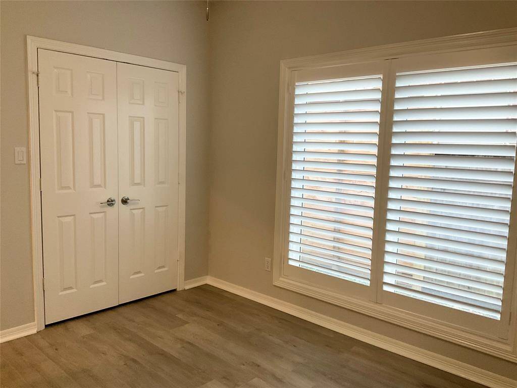 This room features neutral walls, wood flooring, a double-door closet, and large windows with plantation shutters, offering ample natural light.