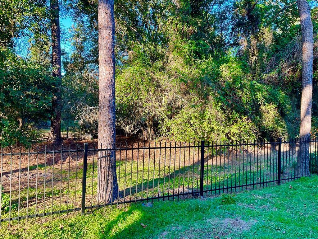 This photo shows a backyard with a black wrought iron fence bordering a wooded area. The space is 5 wooded acres owned by MUD 19.  There is a clean water plant, no noise, tons of privacy and the 5 acres will remain undeveloped. The home or streets have never flooded in this community.