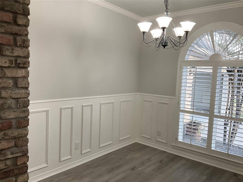 This room features elegant wainscoting, a brick accent wall, and a stylish chandelier. It has a large arched window with shutters, allowing natural light to brighten the space. This room is very flexible and can be used as a dining area, play area, 2nd home office in a very open floor plan.