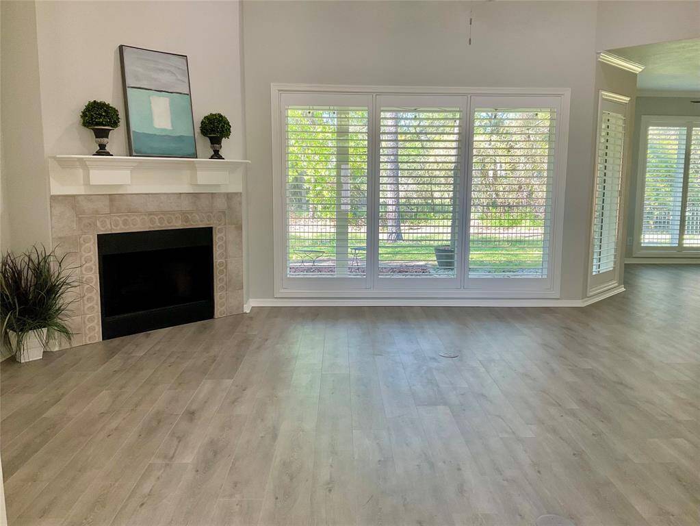 A bright and airy living room features large windows with plantation shutters, offering a view of the outdoors. It includes a cozy gas log fireplace with a stylish mantle, complemented by modern flooring. The view outdoors is stunning!  Owned by MUD 19 with a clean water treatment plant the 5 acres will not be developed.
