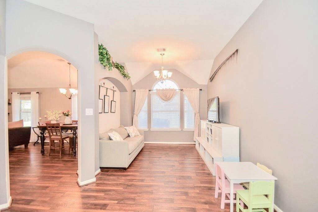 Bright, open-concept living space with hardwood floors and neutral walls. Features include large arched windows, a cozy seating area, and a dining area with elegant lighting. Ideal for family gatherings and entertainment.