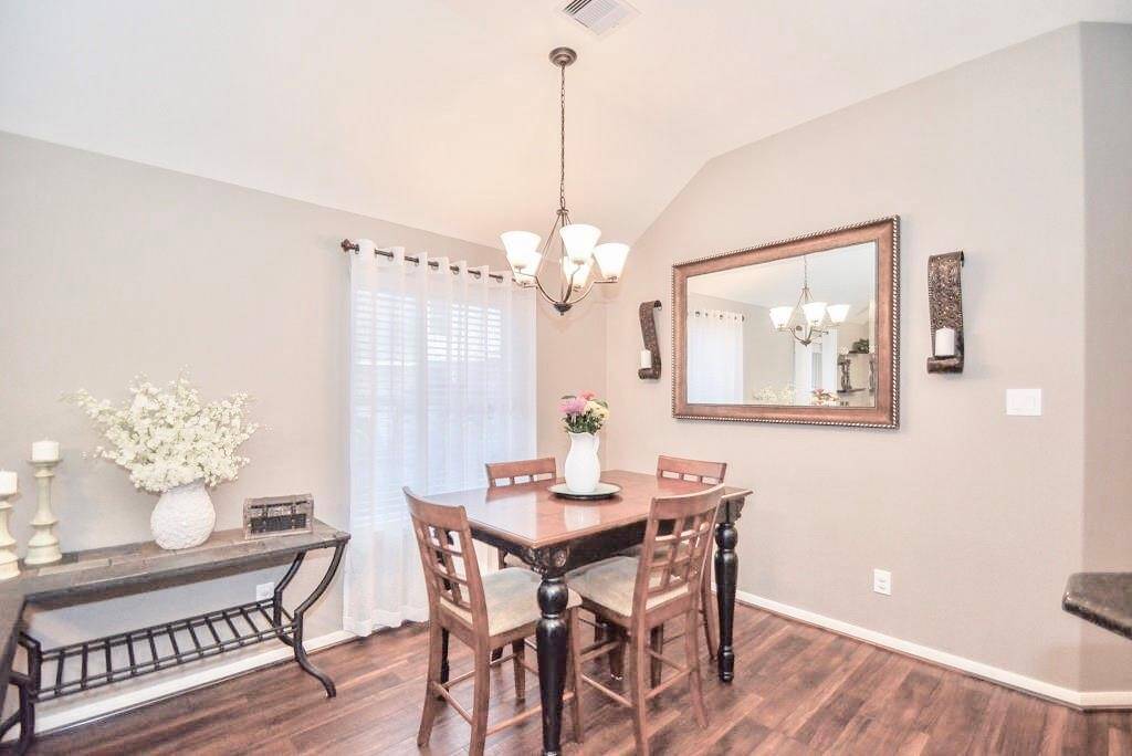 The Dining area features warm wood flooring and neutral walls, creating a cozy atmosphere. It includes a wooden table with matching chairs, a large decorative mirror, and elegant lighting. A side table with decorative accents adds charm, while sheer curtains provide natural light.