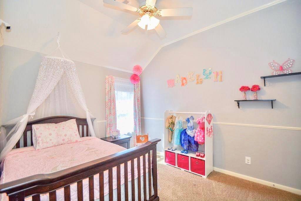 Charming kids' bedroom with soft gray walls and a vaulted ceiling. Features a cozy bed with a canopy, playful decor, and ample natural light from a large window. A ceiling fan provides comfort, and colorful accents add a fun touch.