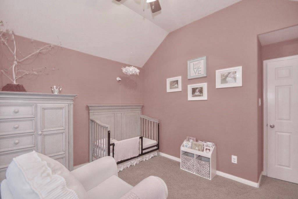 This cozy nursery features soft pink walls, a high ceiling, and a plush carpet. It's furnished with a crib, a comfortable chair, and a dresser, creating a warm and inviting space for a baby.