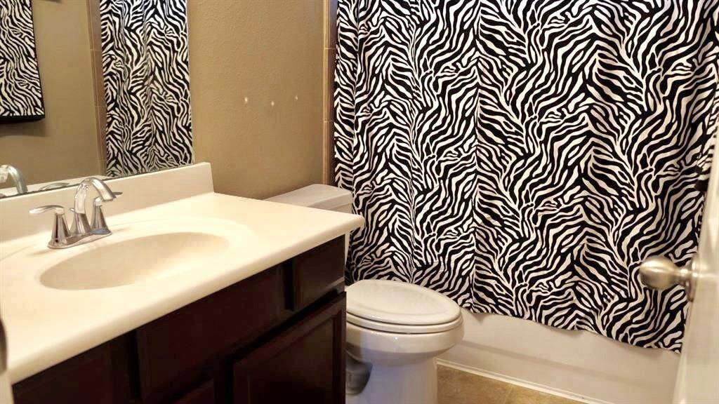 This bathroom features a modern sink with a sleek faucet, dark wood cabinetry, and a bold zebra-patterned shower curtain, creating a stylish and unique space.