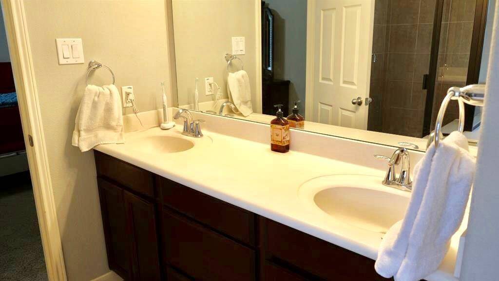 Bright and modern bathroom featuring a double vanity with sleek fixtures, ample counter space, and a large mirror. The room has neutral tones and a glass-enclosed shower, creating a clean and spacious feel.