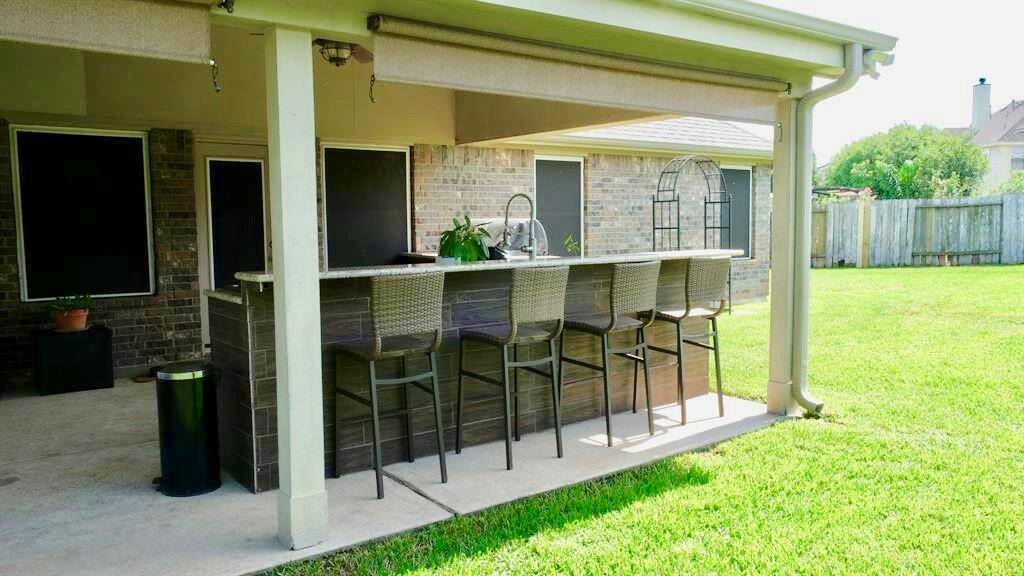 Spacious backyard with a covered patio area featuring a built-in outdoor bar with seating. The area is ideal for entertaining and overlooks a well-maintained lawn.