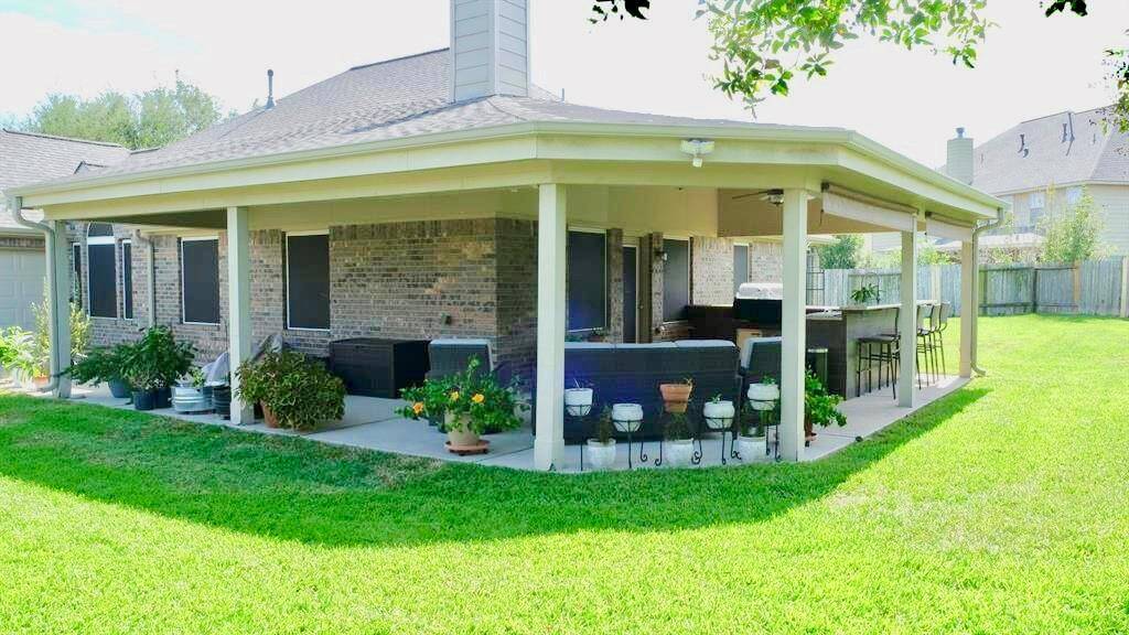 Huge covered patio attached to a brick home. The patio features ample seating, a bar area, and is surrounded by a well-maintained lawn, perfect for outdoor entertaining.