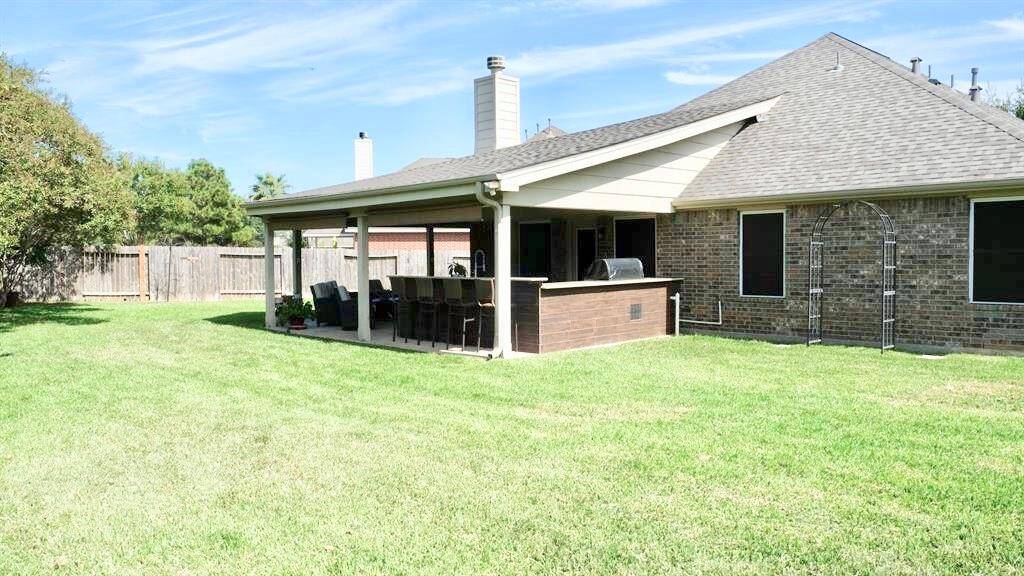 Spacious backyard with a well-maintained lawn, featuring a covered patio area perfect for outdoor dining and entertaining. The brick exterior of the house adds a traditional touch, while the fenced yard offers privacy.