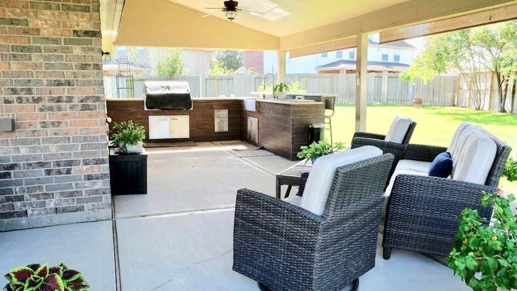 Spacious covered patio with comfortable seating and a built-in outdoor kitchen area, perfect for entertaining. The backyard is fenced and includes a well-maintained lawn, providing a private and inviting outdoor space.