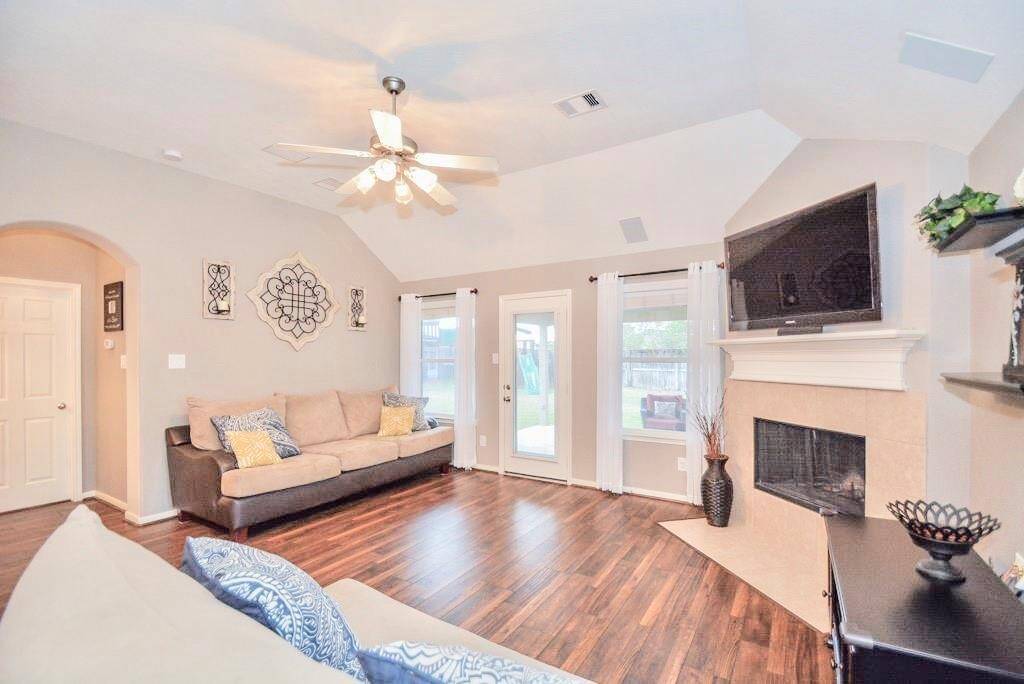 Inviting living room features hardwood floors, a cozy fireplace, and a mounted TV. Natural light fills the space through large windows and a glass door leading to the backyard. The room is tastefully decorated with neutral tones and modern accents.