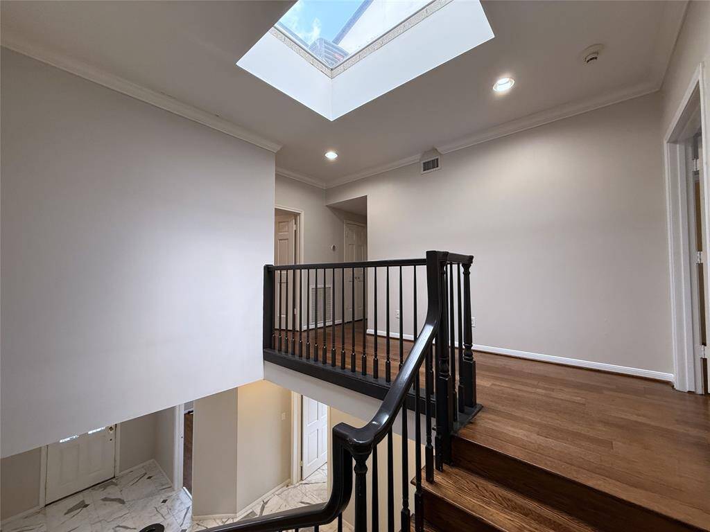 From a skylight, natural light flows into the upstairs hallway and beyond to the entry foyer. At the top of the stairs and and the right is the primary suite.