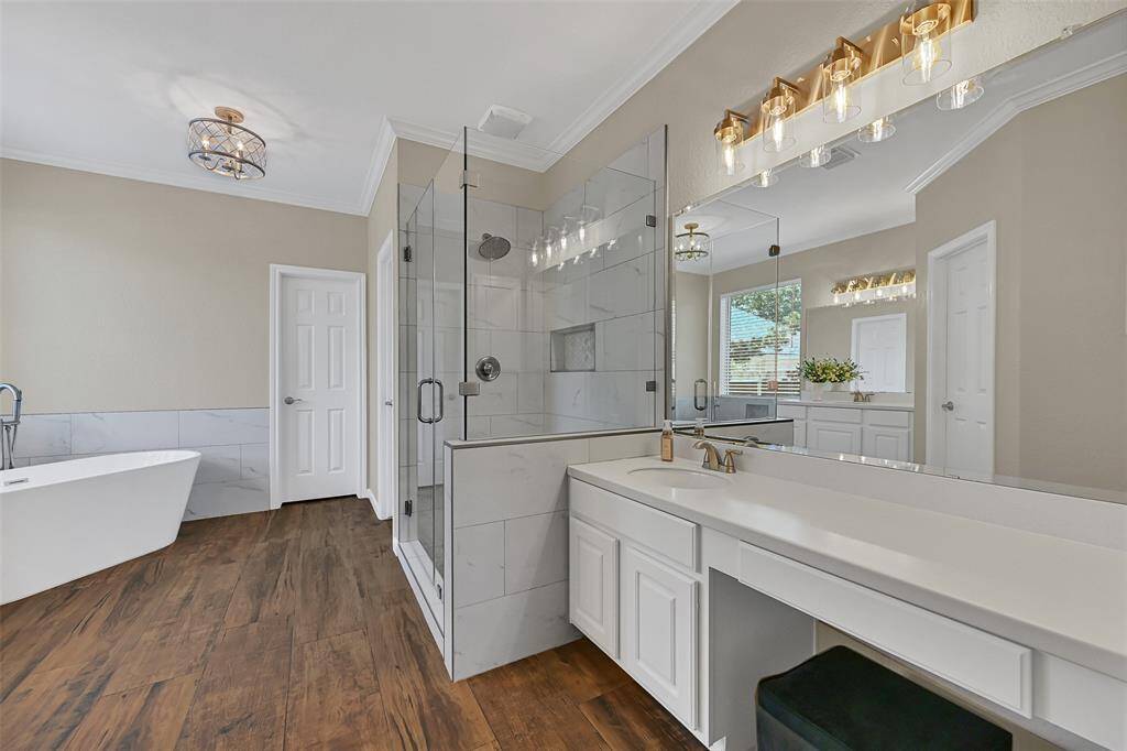 This beautifully renovated primary bath features a freestanding soaking tub & oversized frameless glass shower with a coordinating marble tile surround, double vanities with updated fixtures, and stylish lighting throughout.