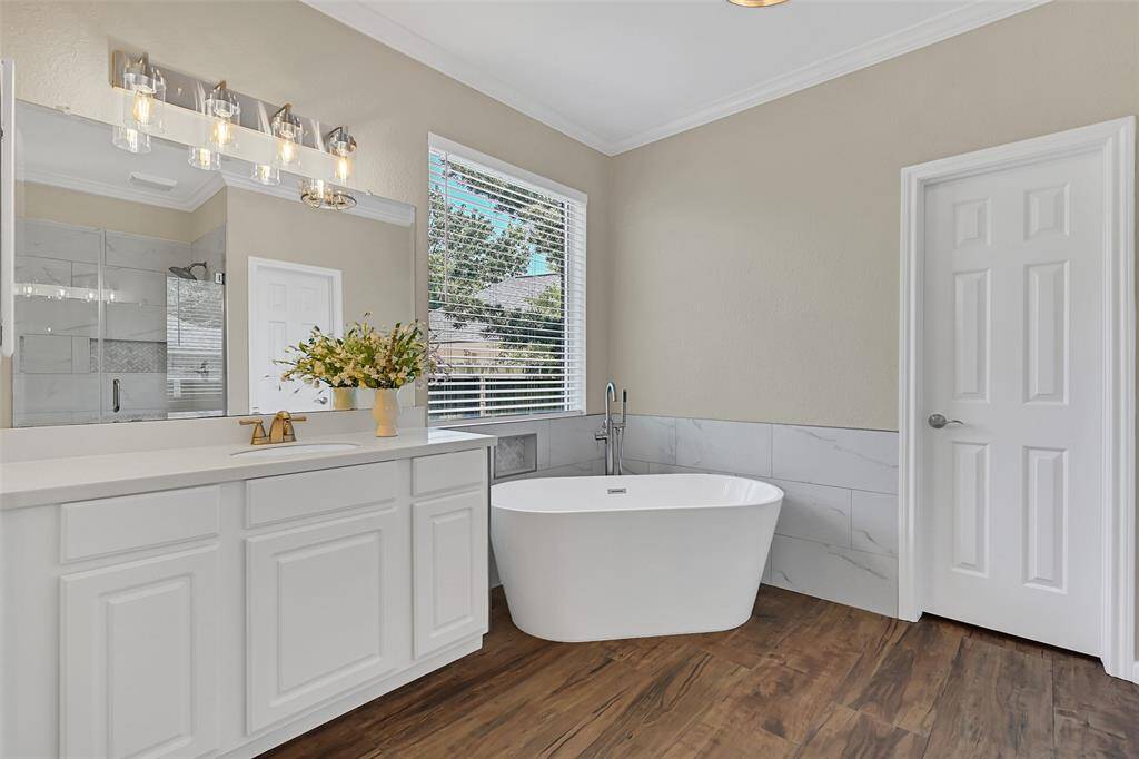 This beautifully renovated primary bath features a freestanding soaking tub & oversized frameless glass shower with a coordinating marble tile surround, double vanities with updated fixtures, and stylish lighting throughout.