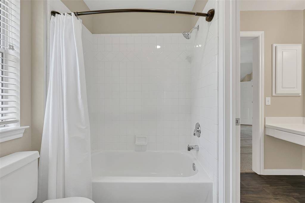 Jack & Jill bathroom designed for functionality and privacy, offering dual vanities with sleek white cabinetry and updated lighting, along with a central bathing area that includes a tiled tub/shower combo and private water closet access from each side.