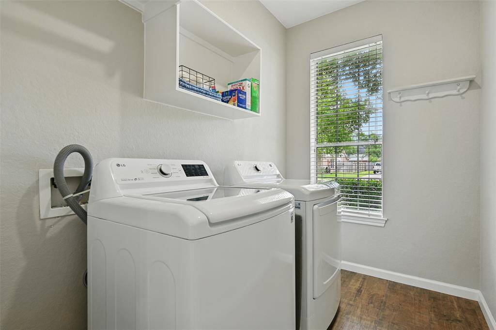 Laundry room located just off the kitchen, featuring a large window for natural light, overhead storage, and stylish wood-look flooring.