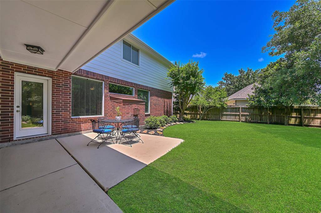 Spacious backyard with a covered patio and extended open-air concrete area, perfect for outdoor dining or entertaining. Mature landscaping and a fully fenced yard provide shade and privacy.
