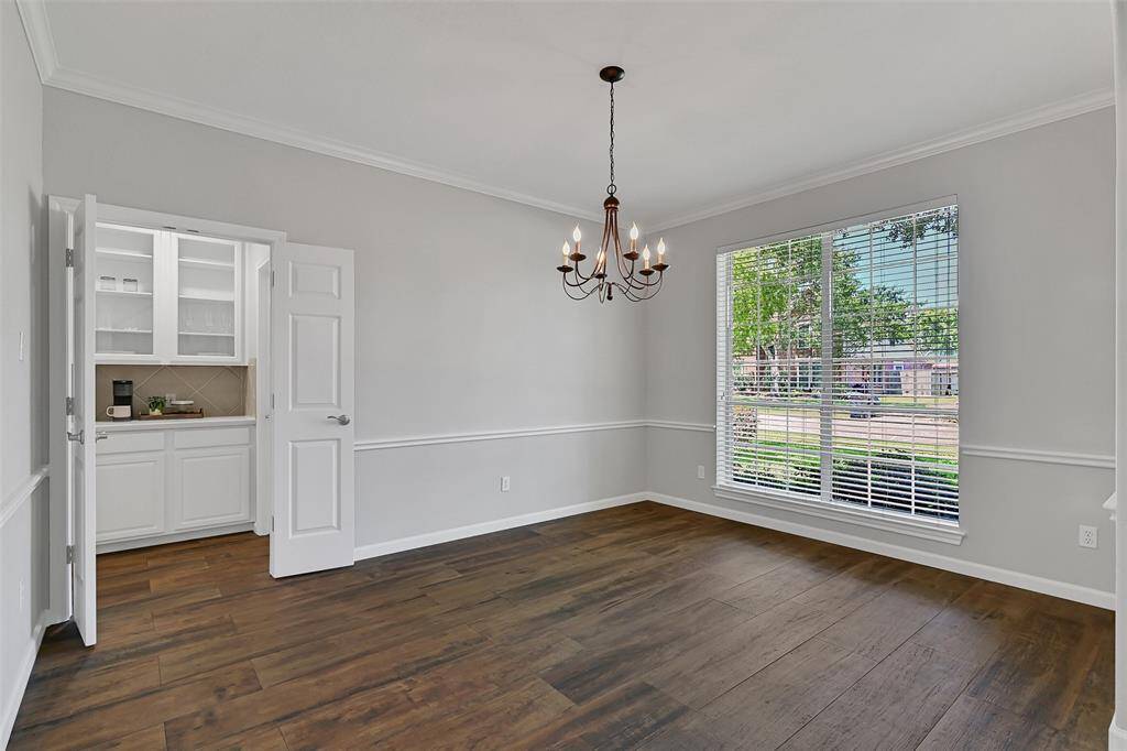 Entertain in this elegant dining room with fresh neutral paint, crisp white crown molding, wood-look tile floors, and a front-facing window for natural light. A peek into the butler’s pantry reveals glass-front cabinets and granite counters.