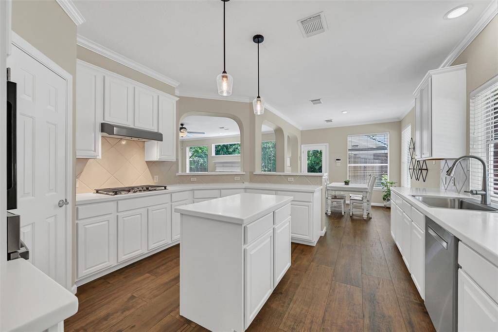 Cooking isn't such a chore in this bright and spacious kitchen with sleek white Corian countertops & crisp white cabinetry to contrast the warm wood-look tile flooring, a center island topped by a pair of stylish pendant lights, and a brand-new gas cooktop & stainless sink.