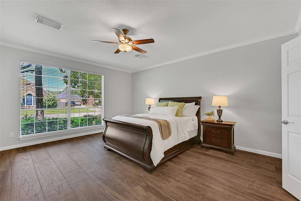Escape to the serenity of this spacious first-floor primary suite that features wood-look tile flooring, soft gray walls with crisp white trim, and an expansive picture window that fills the room with natural light and frames front yard views.