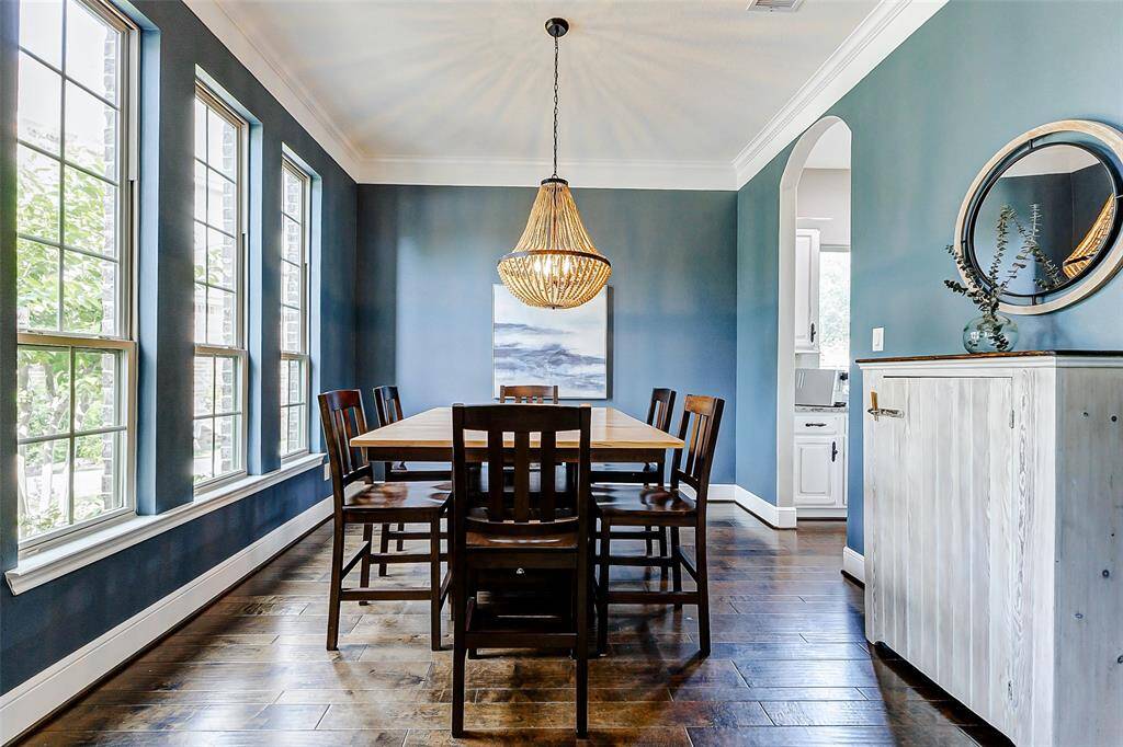 To the left of the foyer, an elegant dining area awaits, featuring tasteful decorator paint, crown molding, and a striking chandelier that creates a dramatic focal point. You also have wood flooring and three expansive floor-to-ceiling windows that offer a view of the front yard, further elevating the space's charm and sophistication.