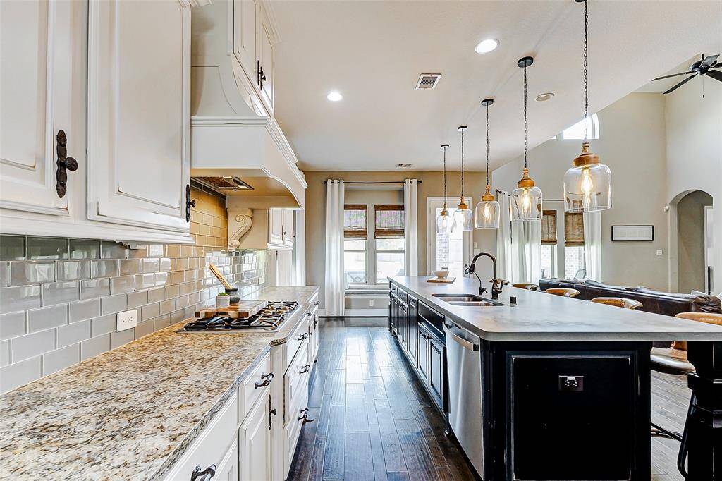 The kitchen is further enhanced by a gas cooktop with a matching vent hood that seamlessly ties into the stunning cabinetry. A neutral subway tile backsplash provides a timeless backdrop, while the dark-toned island contrasts beautifully with the crisp white cabinetry along the wall, creating a perfect balance of style.