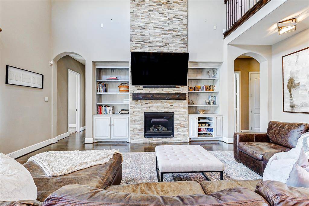 Step into the expansive living room, where soaring two-story ceilings create a light, open atmosphere. A dramatic floor-to-ceiling stacked stone fireplace, flanked by custom built-in shelving and cabinetry, serves as the room’s stunning focal point, enhancing the sense of height and grandeur.